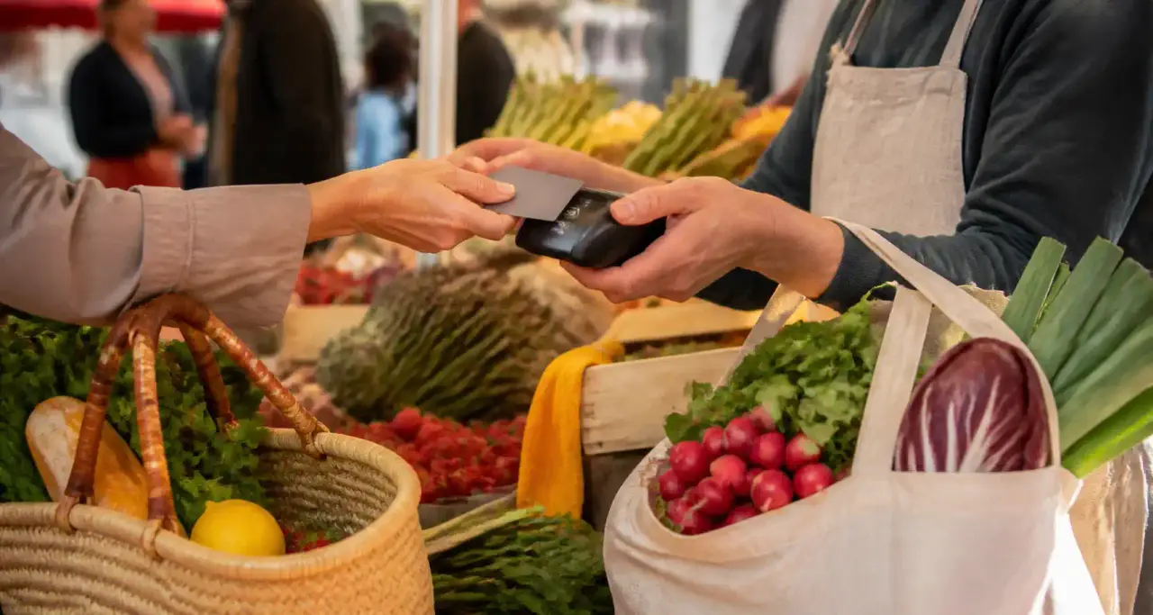 Paiement sans contact par carte bancaire sur un étal de marché, panier de courses rempli de fruits et légumes
